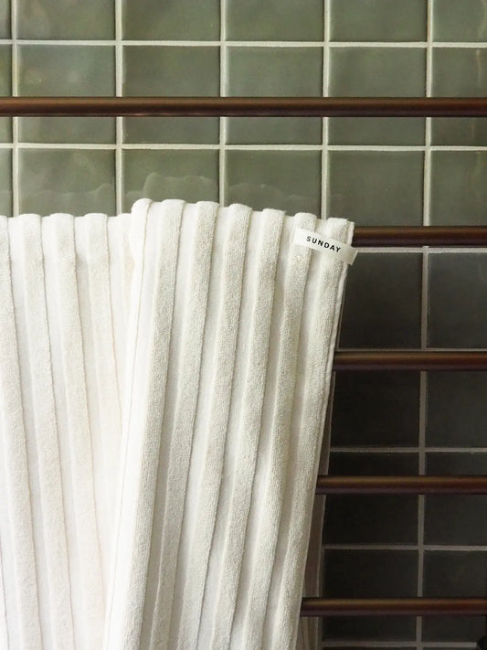 Sunday Supply Co. home towels draped over a wooden rail against sage green tiles