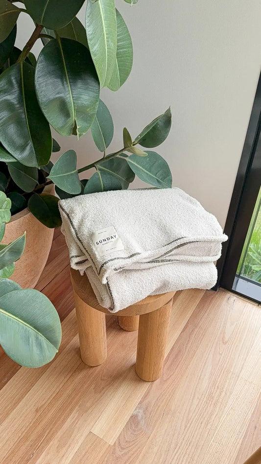 Folded knitted home blankets beside a window with greenery in warm light