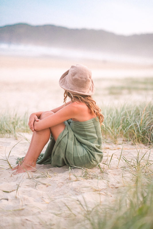 Sunday Supply Co. beach towel wrapped around a person seated on the sand