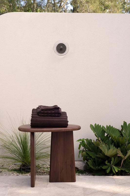 Neatly folded chocolate bath towels on a timber table outdoors