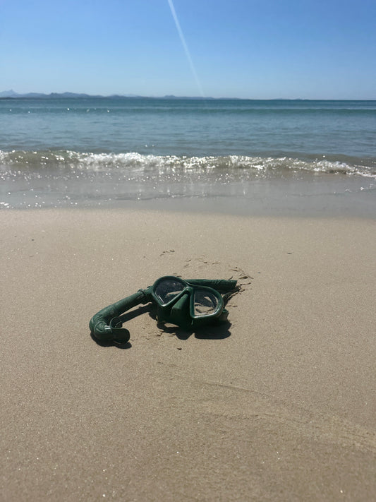 Native mask and snorkel set resting on wet sand beside the ocean