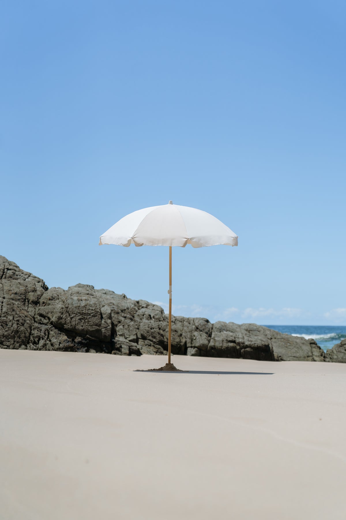Dunes Splice Beach Umbrella on open sand beside coastal rocks