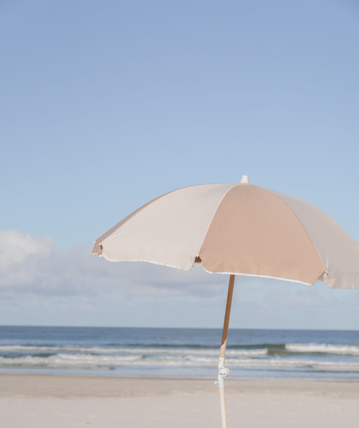 Husk Splice Beach Umbrella with tan and off-white panels beside the ocean