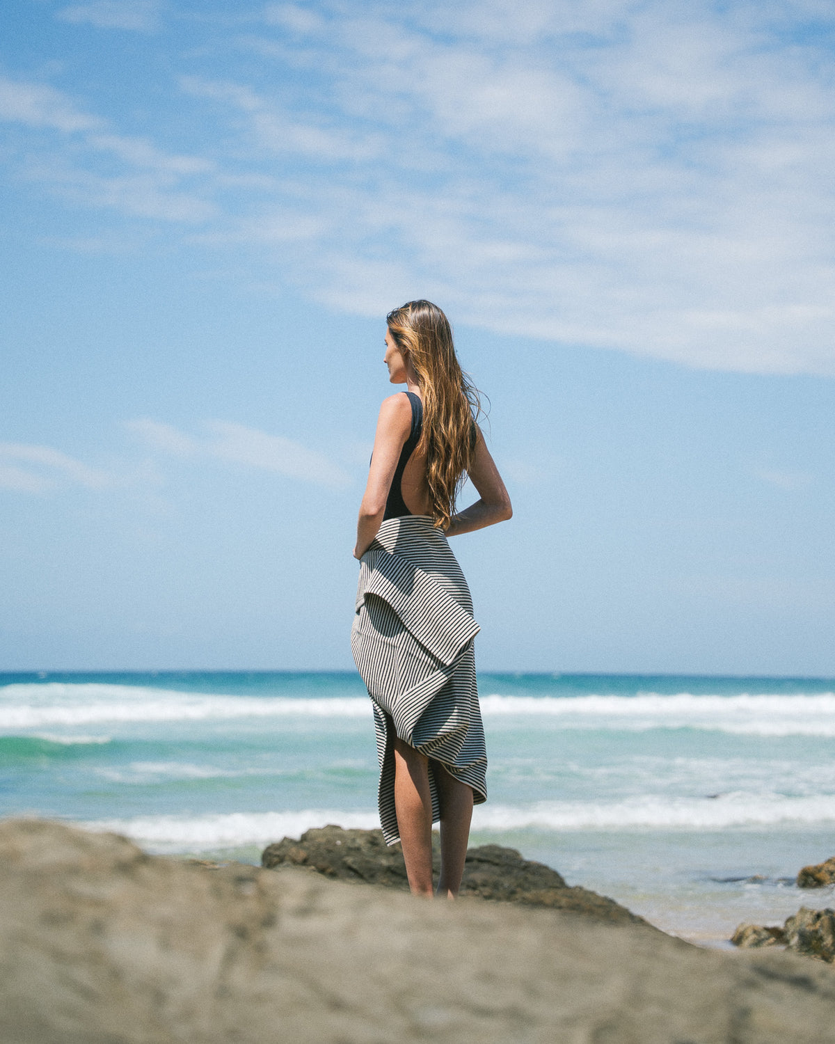 Black striped beach towel worn around the waist on a rocky beach.